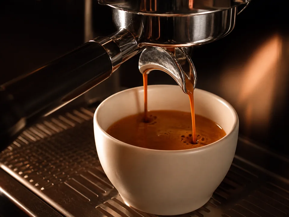 Espresso flowing from a portafilter into a ceramic cup.